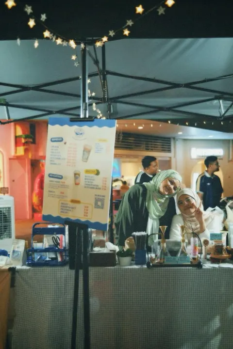 Two members of the Brewprint team smiling behind the stall at night under the string lights