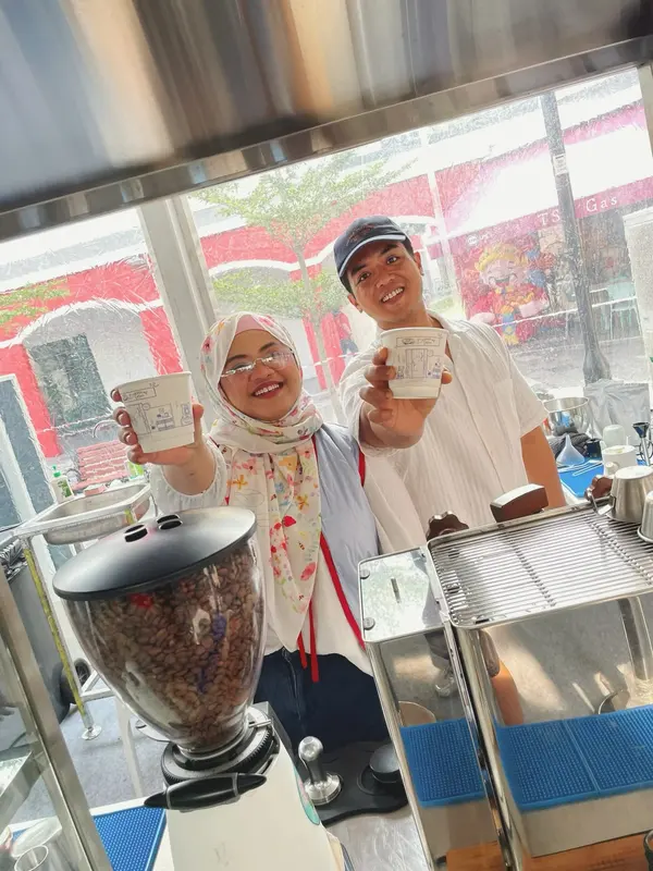 Two of the Brewprint team raising their cups behind the espresso machine and grinder at the Weekend Brew Club pop-up