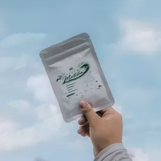 Hand holding a pouch of Brewprint Cloud Matcha against a blue sky